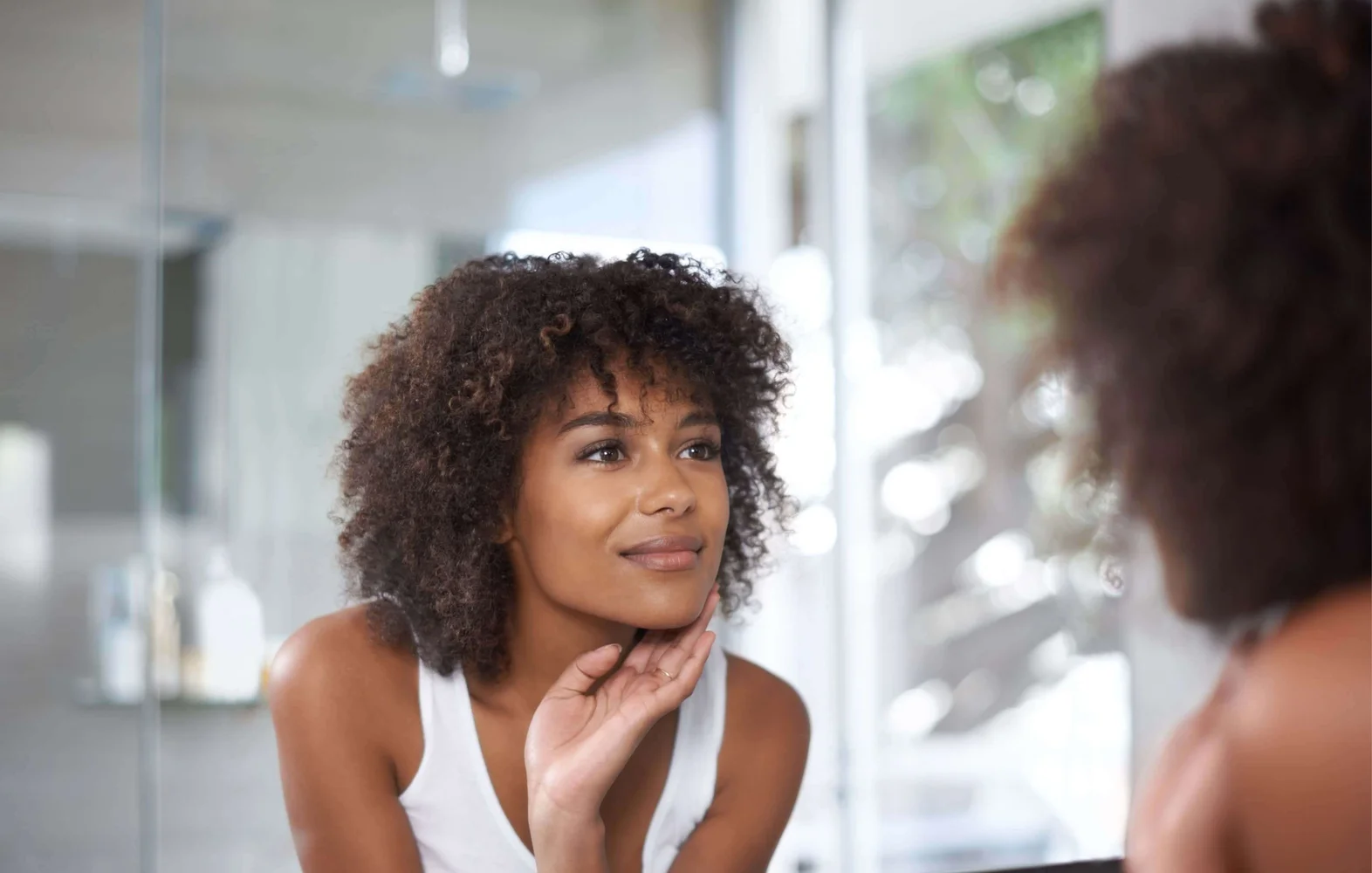 Woman with curly brown hair looking at herself in the mirror